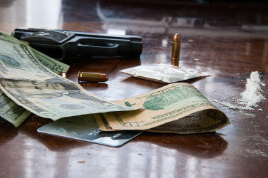 Over a table: a gun, 3 bullets, a bag of cocaine and several dollars spread around