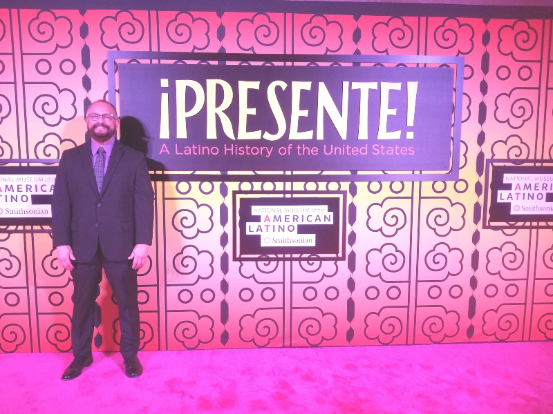 Ricardo López stands next to a sign that says "Presente: A Latino History of the United States"
