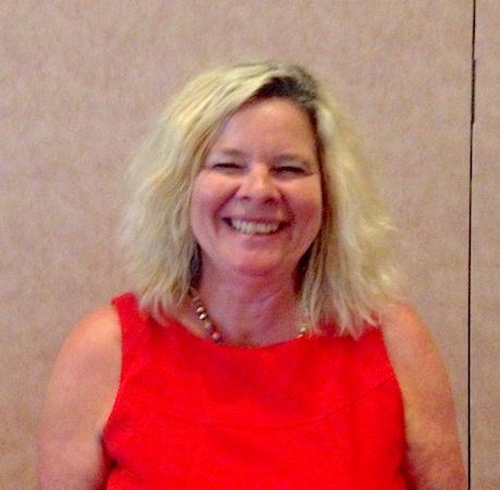 Susan LaVenture smiles broadly while standing indoors. She has blond shoulder-length wavy hair and a sleeveless red dress. She has blond shoulder-length wavy hair and a sleeveless red dress.