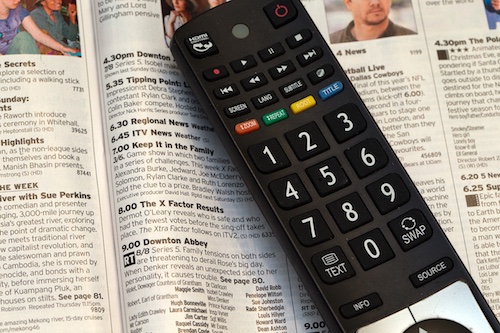 A remote control rests on a page of a TV guide page.