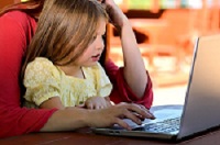 Una niña y una mujer ven la pantalla de un computador portátil