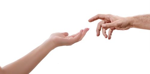 The forearm of a woman extends with the palm of her hand facing up. The hand of a man, with the palm facing down and the index finger slightly bended, approaches the woman's hand.