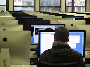 Sala de computadoras. Un hombre ve la pantalla encendida de una computadora.