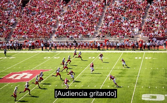 Partido de fútbol americano.  Las graderías están llenas de gente. Subtítulo: Audiencia gritando.