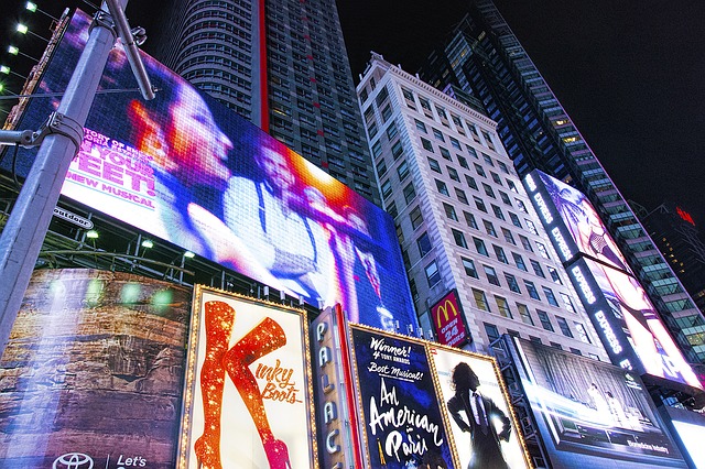 At night, Times Square billboards of the Broadway shows: On Your Feet, Kinky Boots, and An American in Paris