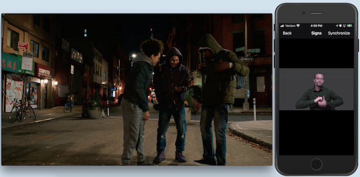 A la izquierda, imagen de 3 jóvenes con chaquetas de invierno de pie en un semicírculo junto a la esquina de una calle. Ven un teléfono que uno de ellos sostiene más abajo del pecho. A la derecha, un teléfono muestra la imagen de un intérprete de ASL haciendo una seña.