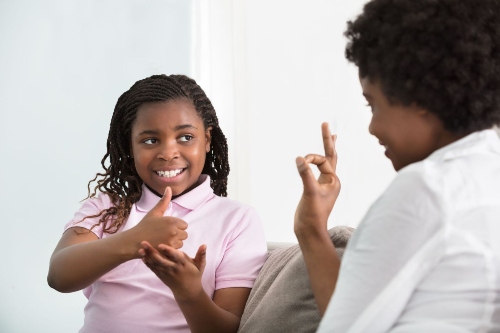 a young girl practices ASL with a woman