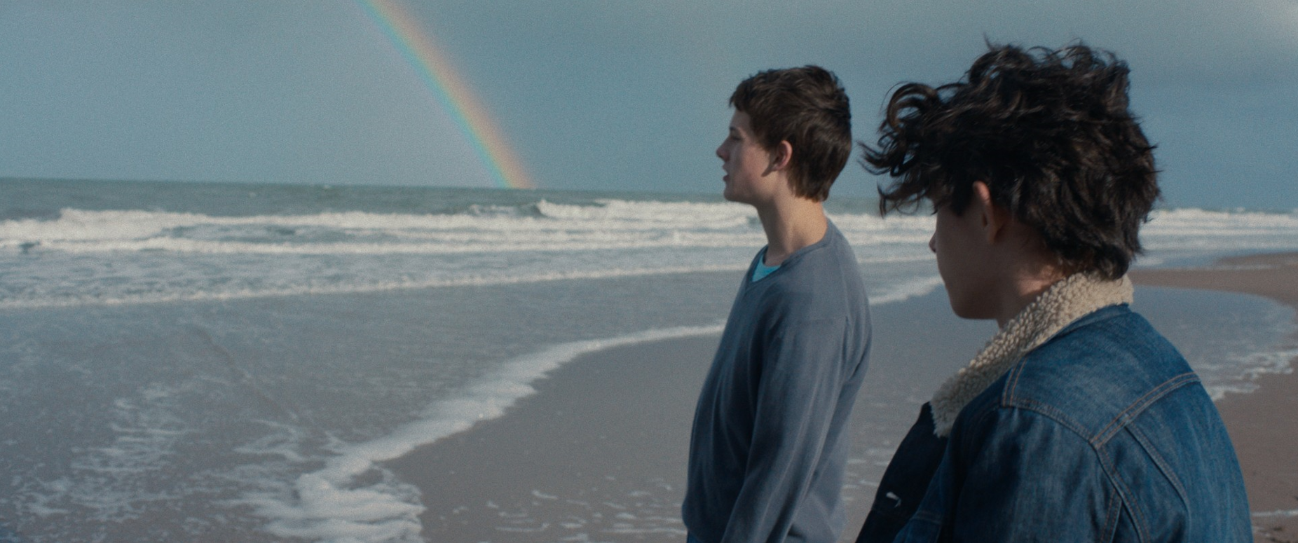 On a beach, two young people look at the sea.