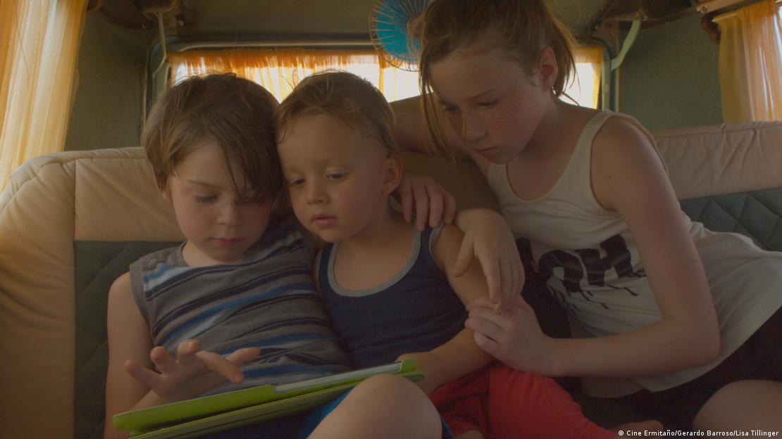Inside a van, three girls look at a tablet.