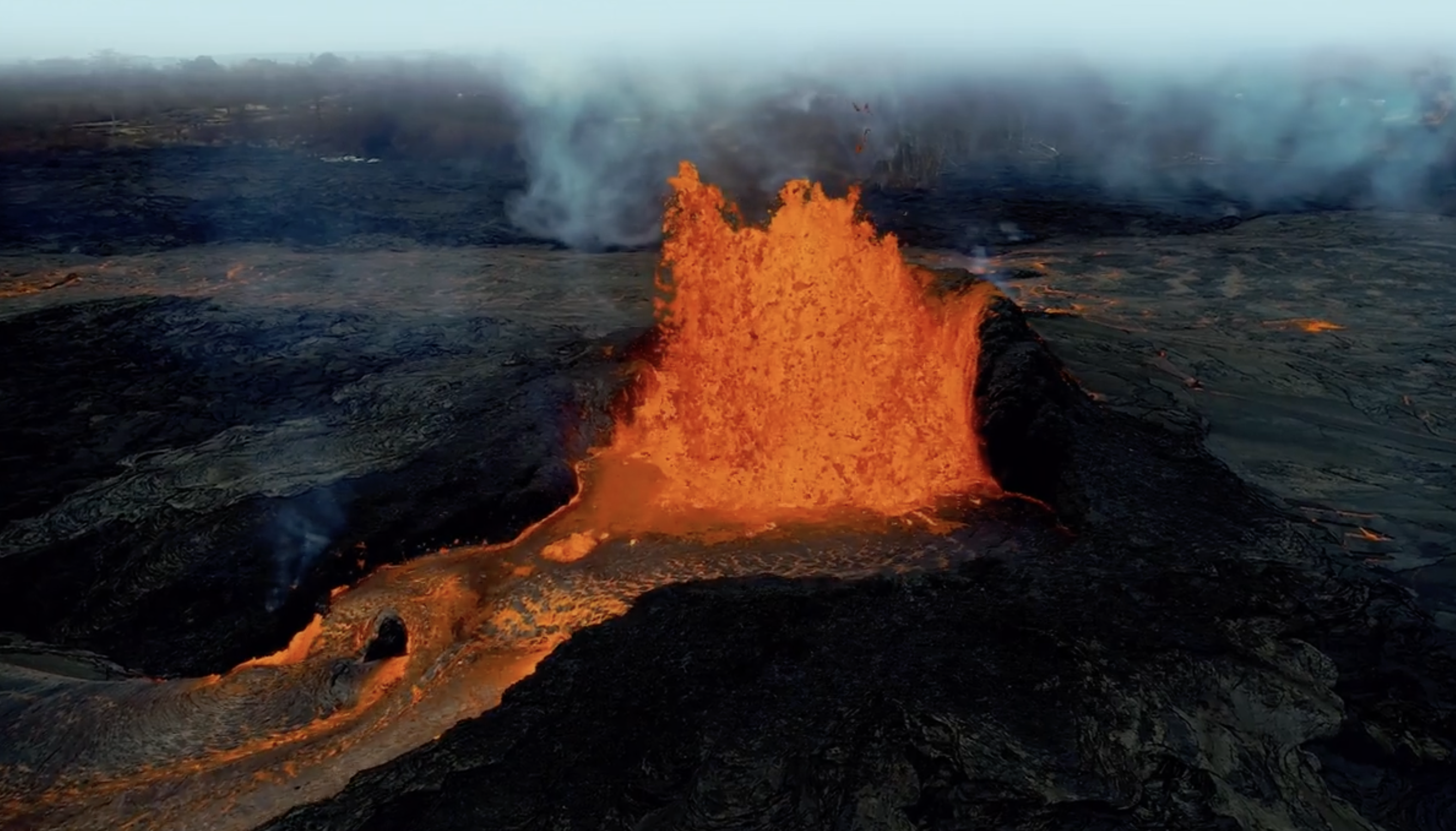 Bright orange lava splashes out from the mouth of a volcano and runs through a path on its side.