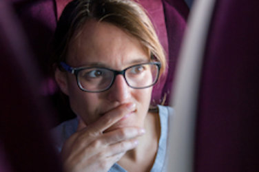 Airplane, Woman with glasses looks forward to the back of a seat in front of her