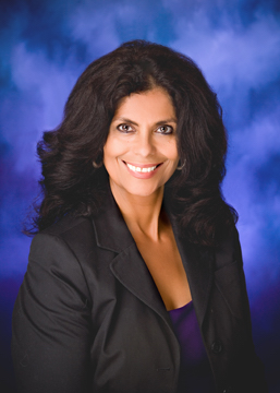 Angela Roth, with abundan black hair, big black eyes smiles. She wears a black jacket over a purple top.