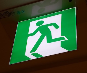 Green evacuation sign with the drawing of a silhouette of a person crossing a door