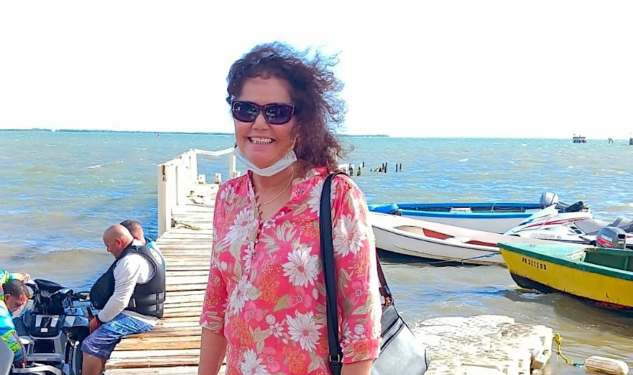 Juanita smiles standing on a pier. The wind blow her hair.
