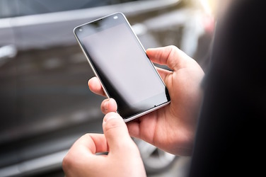 A person holds a smart phone next to a car